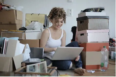 Young woman sitting on the floor using a laptop surrounded by moving boxes — Moving Services in Decatur
