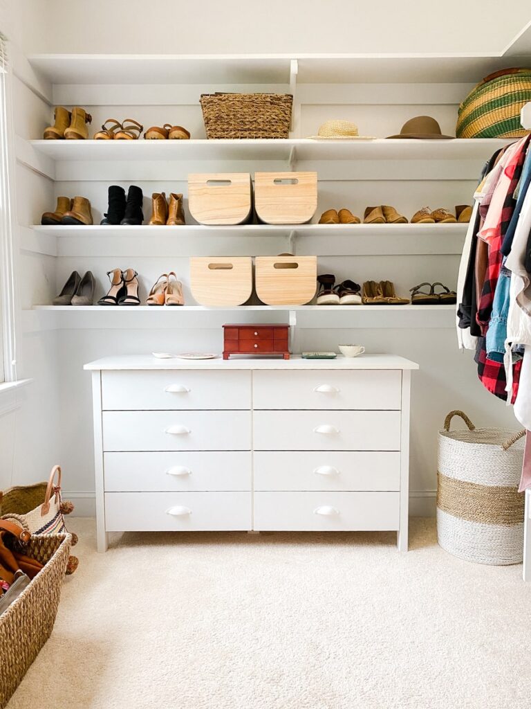 Styled closet shelving with shoes, woven baskets, and a dresser topped with a jewelry box