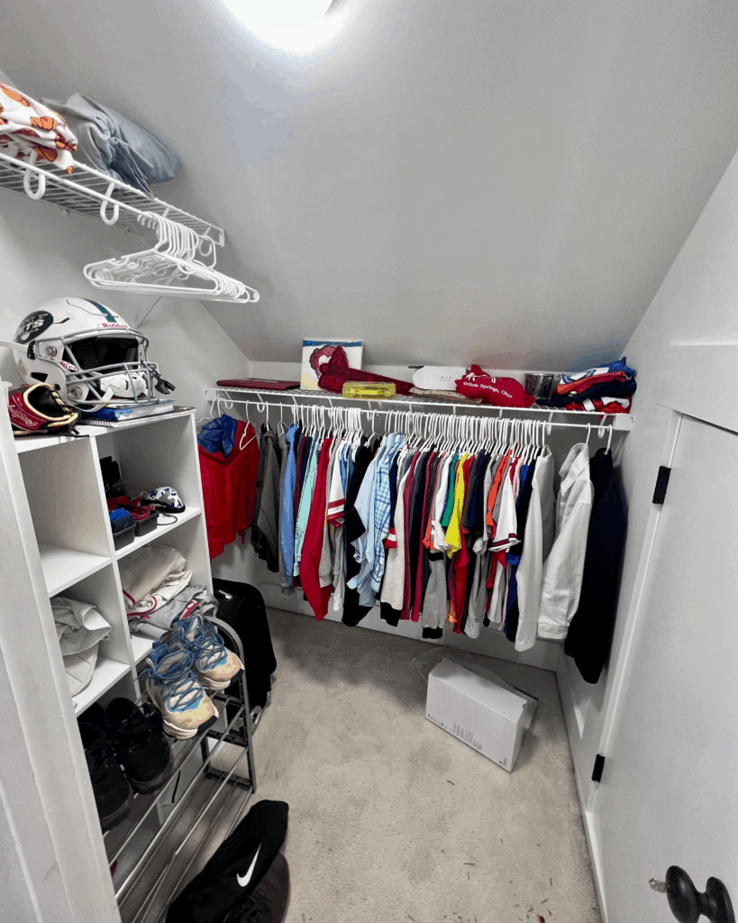 Organized closet with color-coordinated hanging clothes and sports helmet display by Imagine Organizing